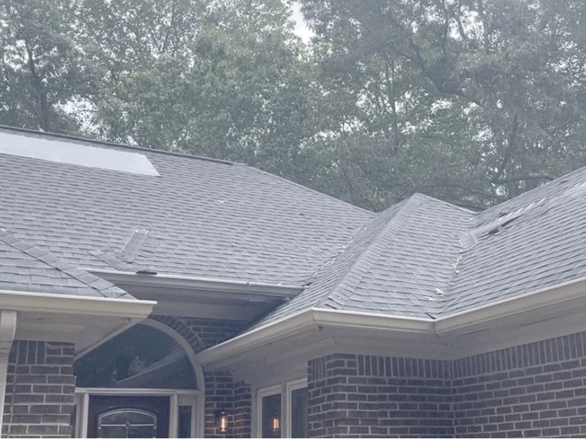 Front elevation over the entry. Patch section on the upper left slope and shingle loss along the hip and ridge lines on the right.
