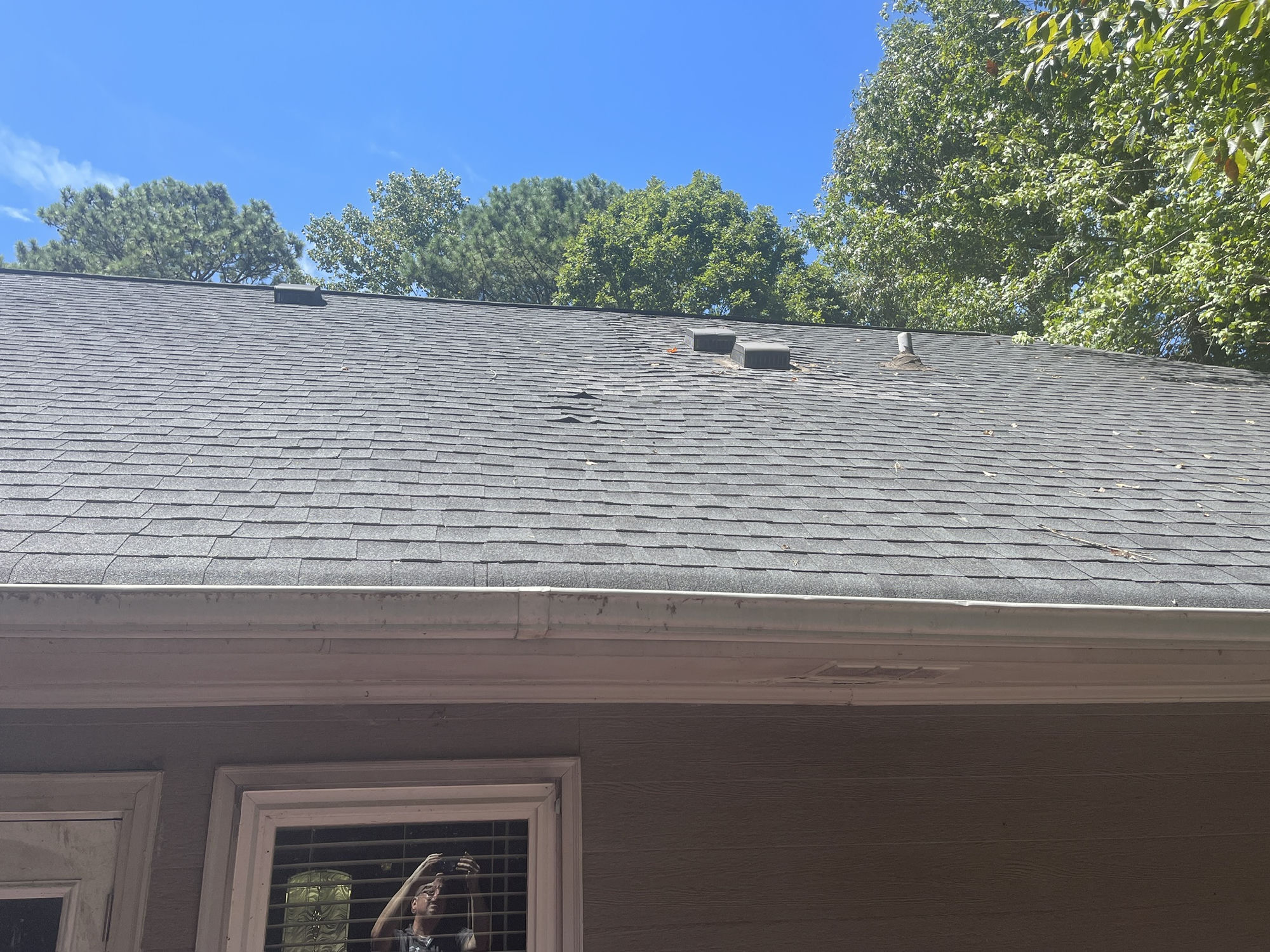 Rear slope at the vent boots. Lifted and creased shingles near the ridge and around the exhaust vents.