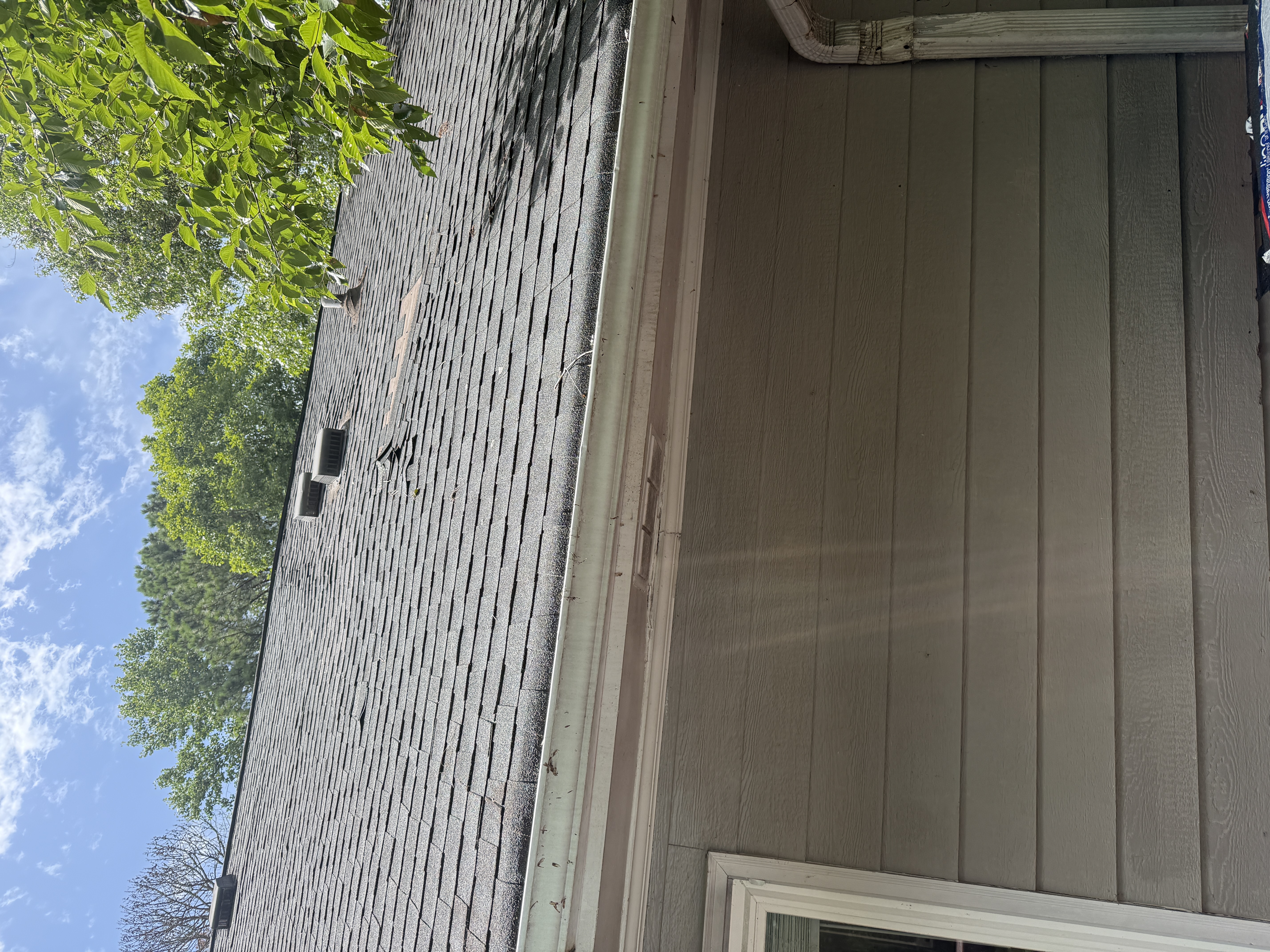 Side slope above the entry, photographed July 19, 2026. Missing and displaced shingles around the exhaust vents with exposed underlayment mid-slope.