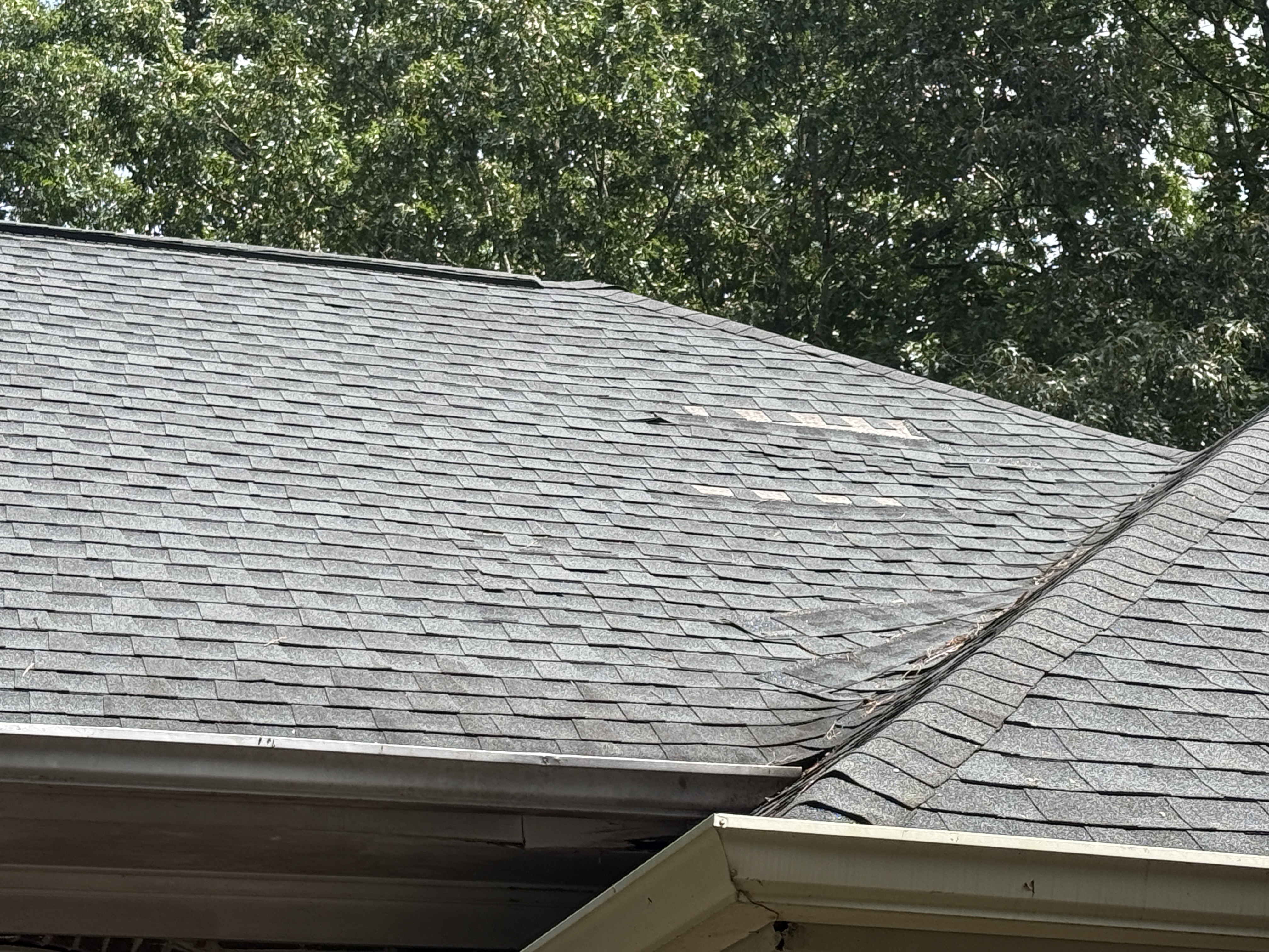 July 19, 2026. Whole courses slid downslope and curling away at the valley, bare spots up the slope. This is the roof Servpro installed in 2018, as it stands today.